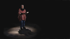 A man in a striped poncho standing in the dark.