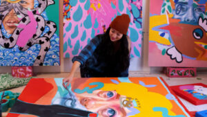 Artist painting a colorful canvas in a studio, surrounded by vibrant, abstract artwork.