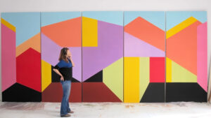 A person stands in front of a large, colorful geometric abstract painting on a wall.