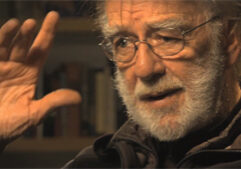 An older man with glasses and a beard gesturing.