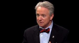 A man in a suit and bow tie talking on a black background.