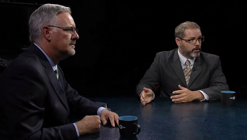 Two men sitting at a table talking to each other.