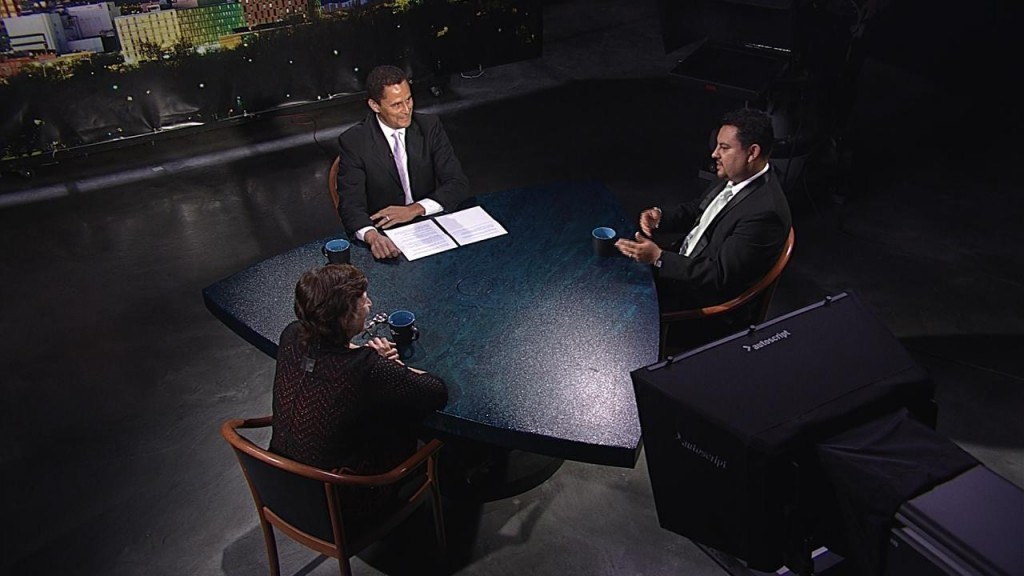 Three people sitting at a table in front of a camera.