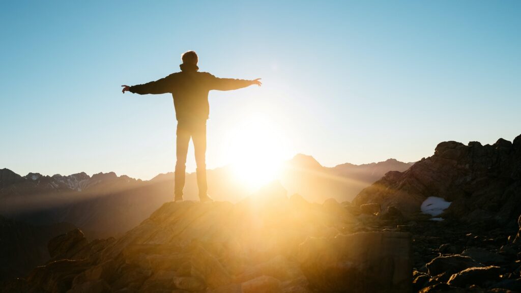 A person stands in a rocky, mountainous range, spreading their arms out.