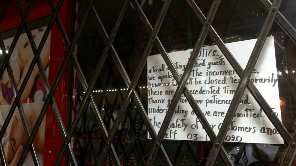 A storefront with a closing notice on the window, and a gate over that.