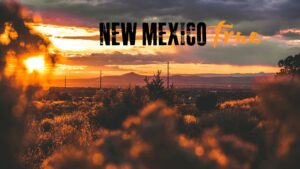 Composite of logo for New Mexico True in front of a view of the desert at sunset.