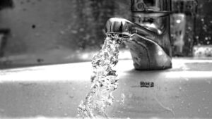 A black and white photo of a faucet gushing water into a sink.