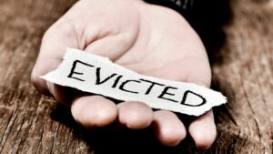 A persons hand resting on a piece of wood palm up holds a piece of paper that says "Evicted."