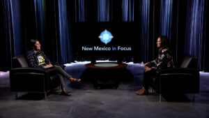 Two women sitting in chairs on a stage with the words new mexico focus.