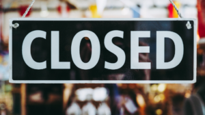 A black and white "CLOSED" sign hanging in front of a blurry background.