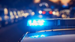 Close-up of a police car with flashing blue lights at night, with blurred cars and street lights in the background.