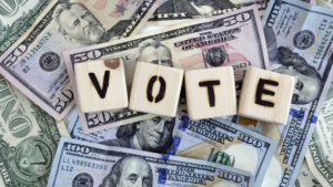 Wooden blocks spelling "VOTE" on a background of various denominations of U.S. dollar bills.