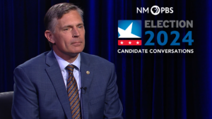 A man in a suit sits in front of a blue curtain. Text reads "NM PBS Election 2024 Candidate Conversations.