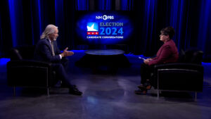 Two people sitting across from each other in a TV studio, discussing the 2024 election. The backdrop displays "NMPBS Election 2024 Candidate Conversations.