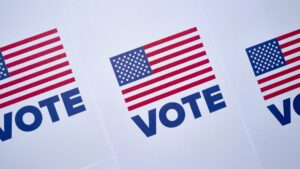 Image of the U.S. flag above the word "VOTE" repeated three times on white paper.