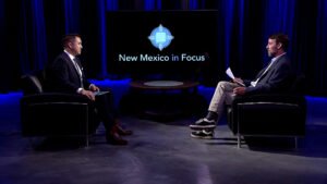 Two men sit facing each other on a TV set with "New Mexico in Focus" displayed on a screen in the background.