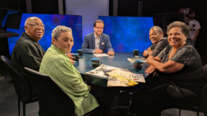 Five people seated around a table in a discussion setting with blue background.