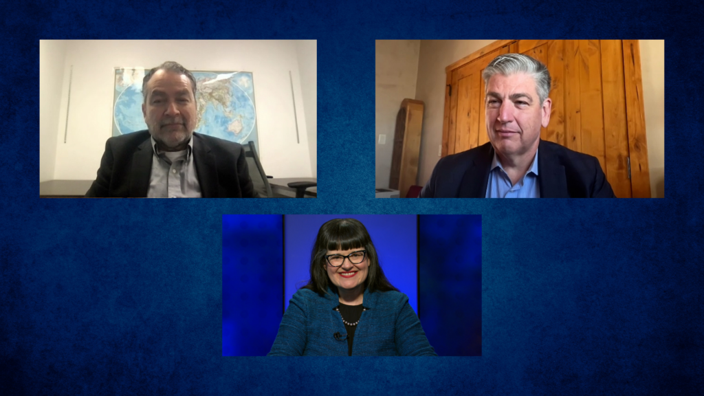 Three people in a video call setup. Two men in separate panels above, with a map and wooden wall backgrounds. A woman below, dressed in blue, smiles in front of a blue backdrop.