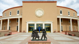 Round government building with a large seal above the entrance. Bronze statue of children dancing in the foreground. Cloudy sky.