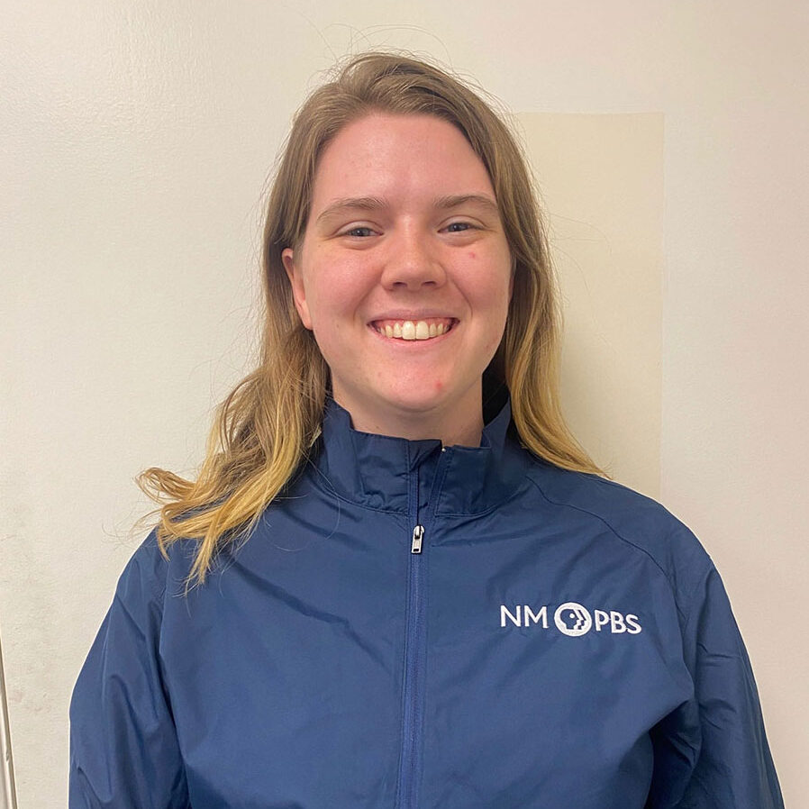 Person smiling, wearing a blue NM PBS jacket, standing against a plain background.